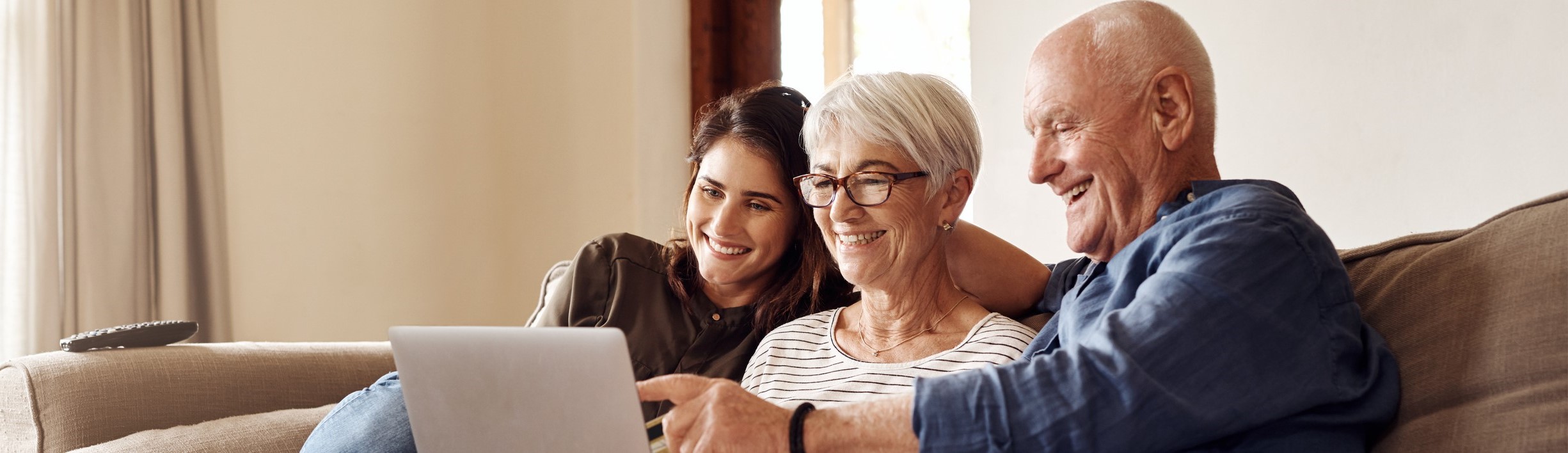 Elderly couple with adult daughter sitting on lounge looking at a laptop